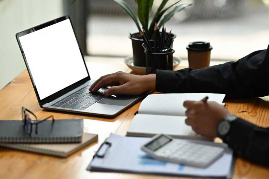 An email copywriter using a laptop and writing notes in a journal.