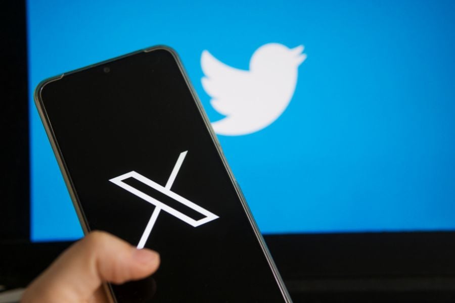 X on phone screen, twitter bird in background